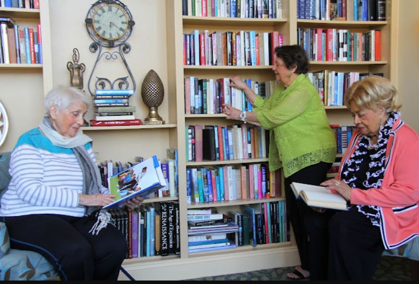 People in a library setting, reading and organizing books on the shelves.