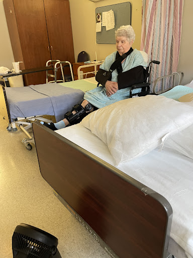 An elderly patient seated in a wheelchair in a hospital room, surrounded by medical equipment and furnishings.