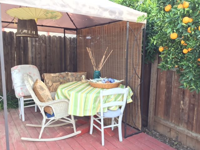 A cozy outdoor patio with a rocking chair and table under an umbrella, next to a lemon tree.