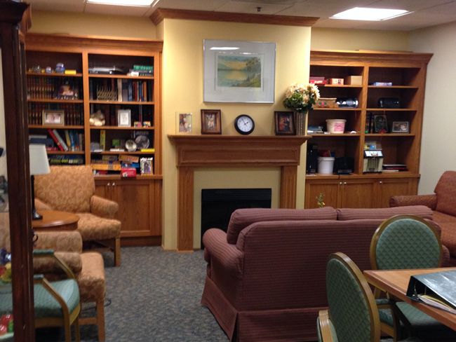 A cozy library room with a fireplace, bookshelves, and comfortable seating.