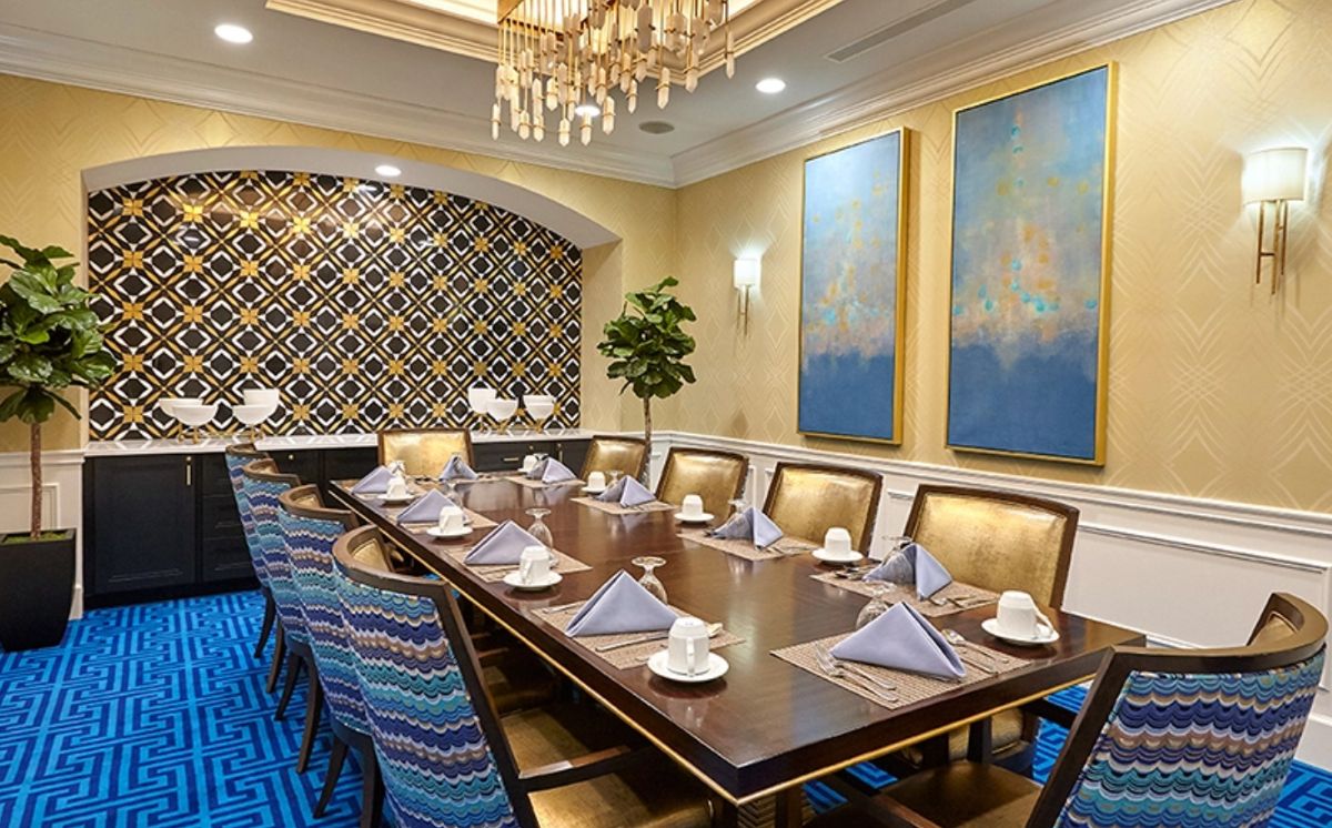An elegantly decorated dining room with a large table set for a formal gathering, featuring a chandelier and decorative artwork.