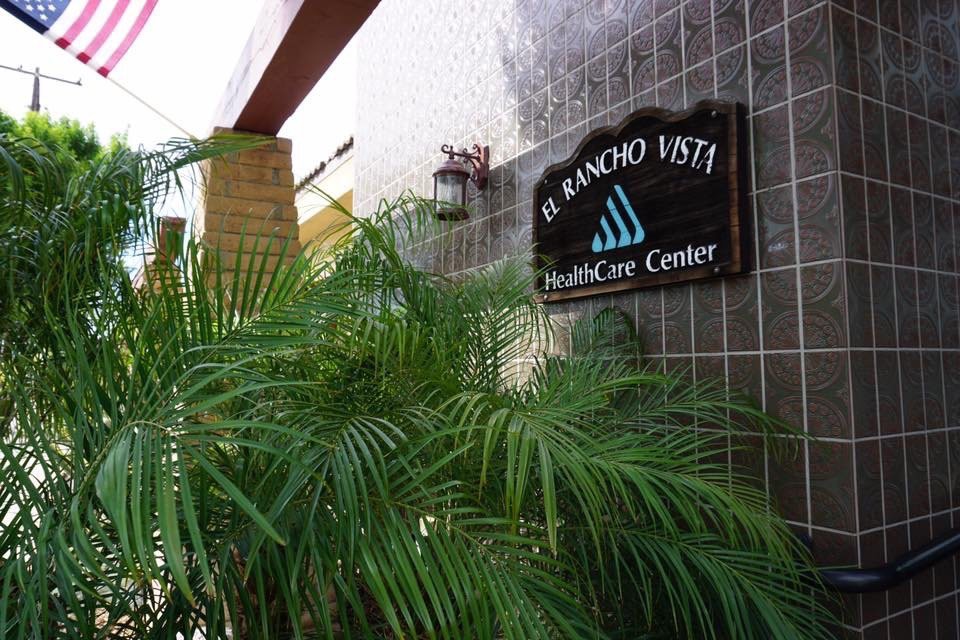 Entrance to El Rancho Vista Healthcare Center surrounded by lush greenery.