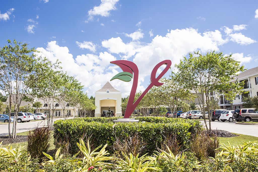 A modern sculpture amidst a well-landscaped entrance to a shopping center on a sunny day.