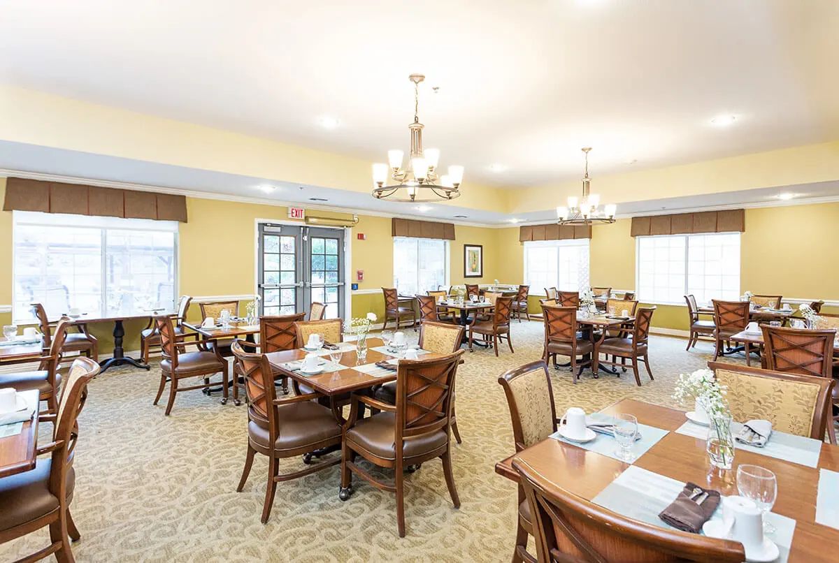 A spacious dining room with neatly arranged tables and chairs, illuminated by chandeliers.