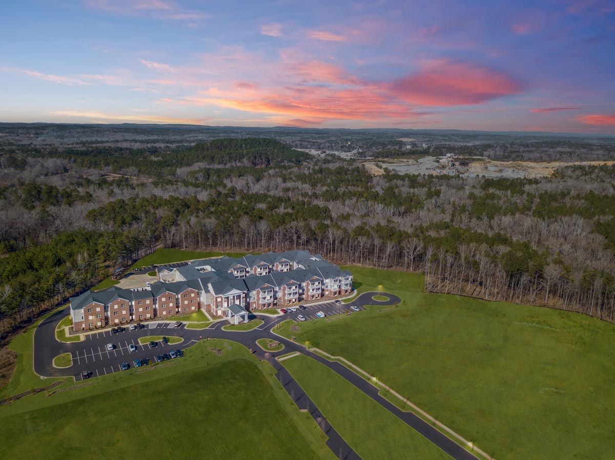 Aerial view of a modern building complex surrounded by lush greenery and a vibrant sunset.