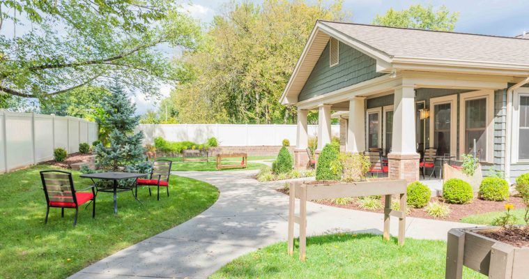 A cozy house with a well-maintained garden and a winding pathway, surrounded by lush greenery and outdoor seating.