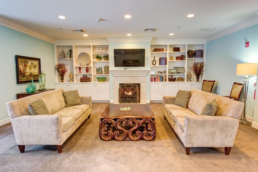 A cozy living room with elegant furniture, featuring sofas, a decorative coffee table, built-in shelves, and a fireplace topped with a television.