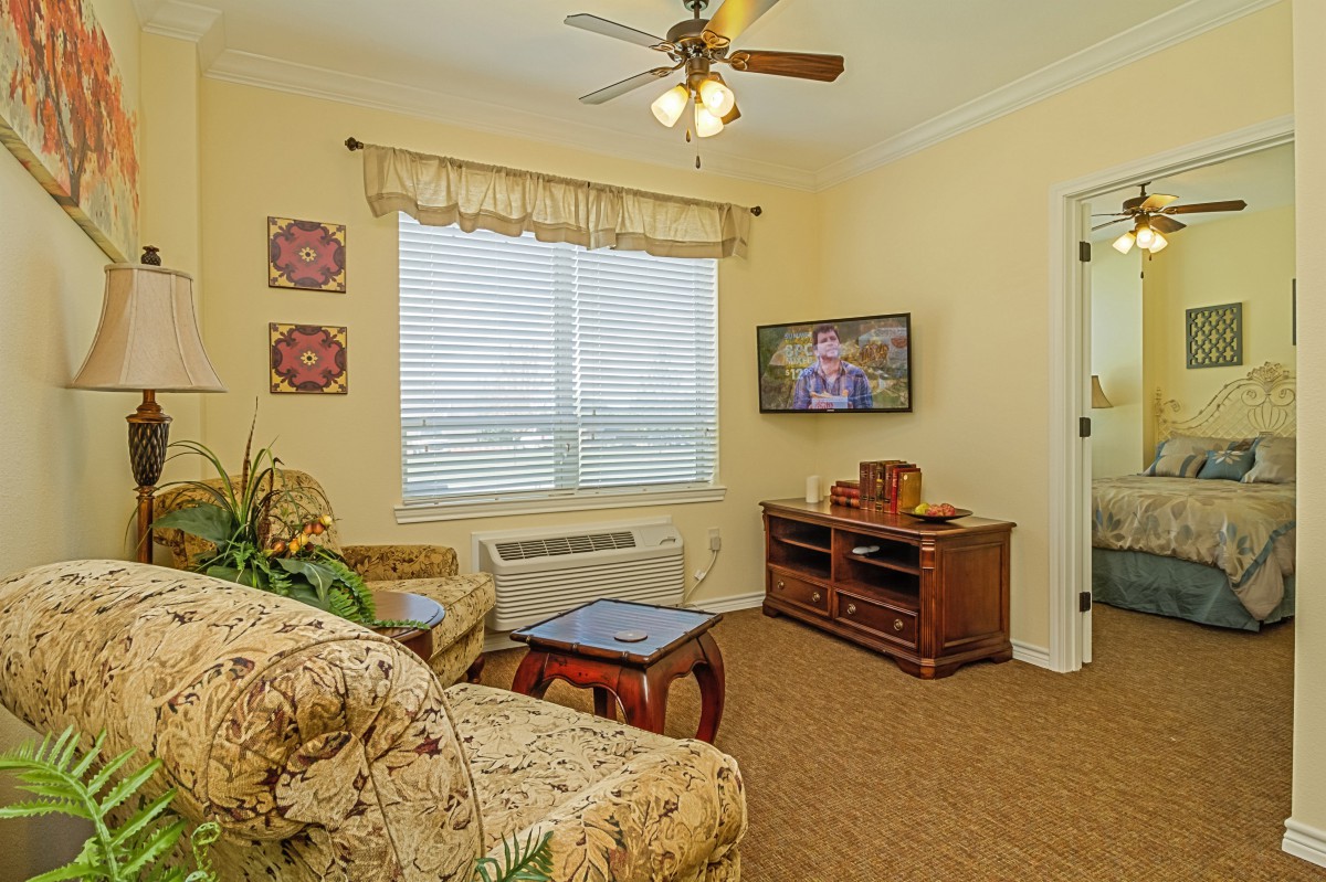 A cozy living room with a sofa, coffee table, and television, featuring warm decor and a ceiling fan.