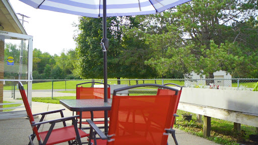 A cozy outdoor setup featuring red patio chairs and an umbrella, surrounded by lush greenery.