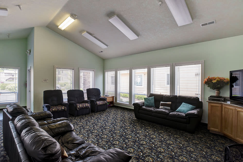 A spacious living room with multiple sofas and armchairs, featuring large windows and a patterned carpet.