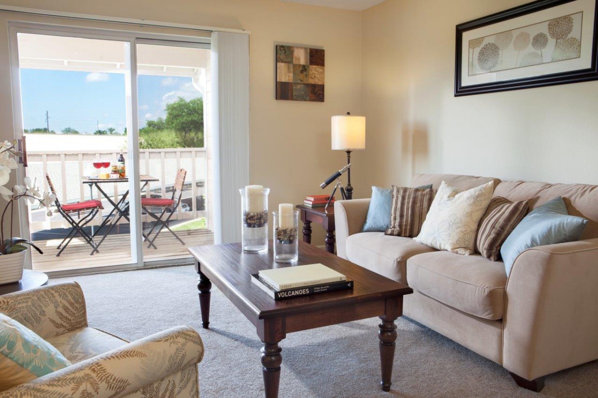 A cozy living room with a beige sofa, wooden coffee table, and a sliding glass door leading to a patio.