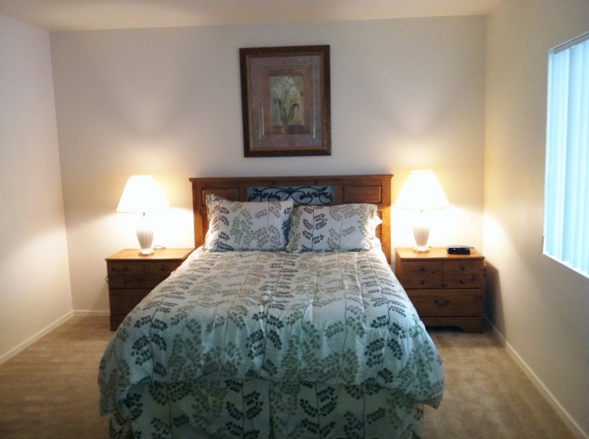 A cozy bedroom featuring a neatly made bed with patterned bedding, flanked by two nightstands with lamps and a framed artwork above the headboard.