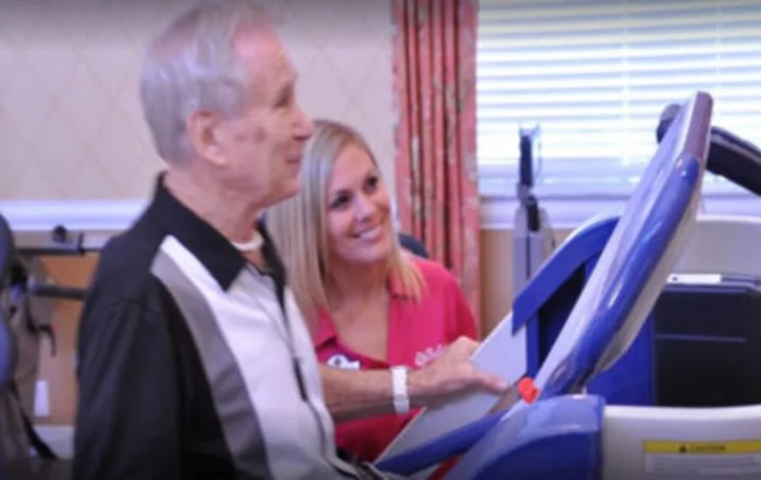 An elderly man receives assistance with medical equipment in a healthcare setting.