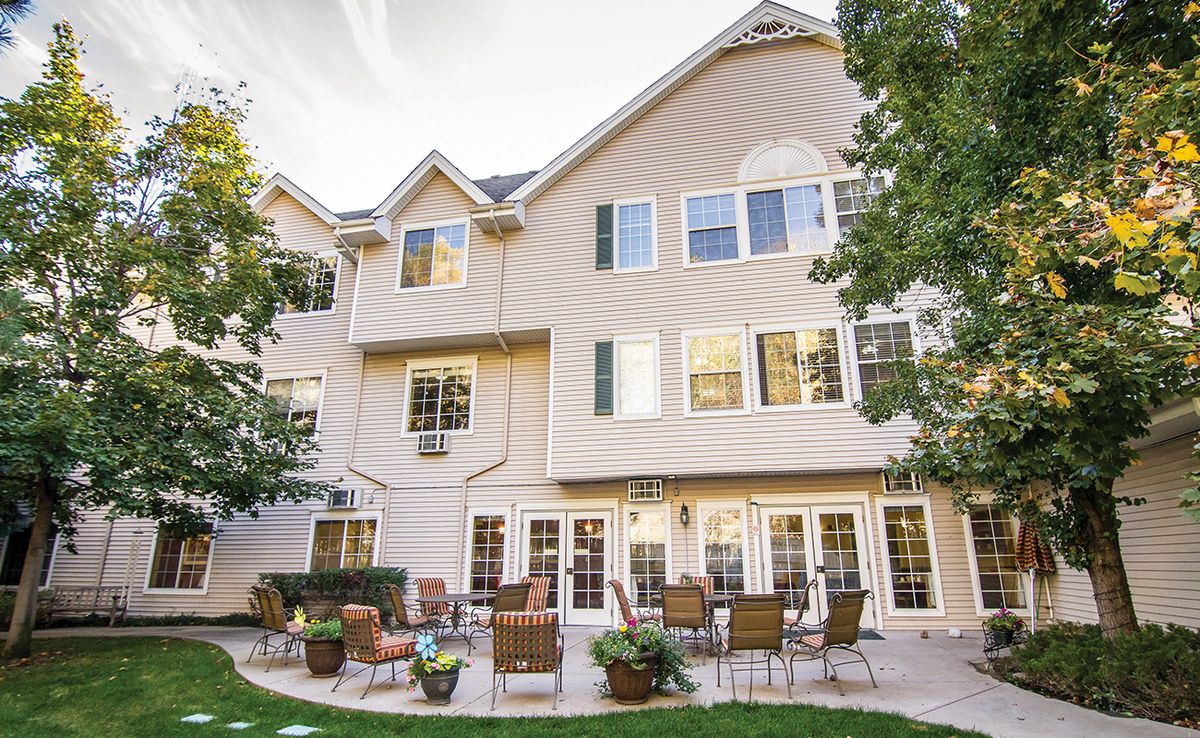 A cozy backyard patio area with seating arrangements adjacent to a multi-story house.