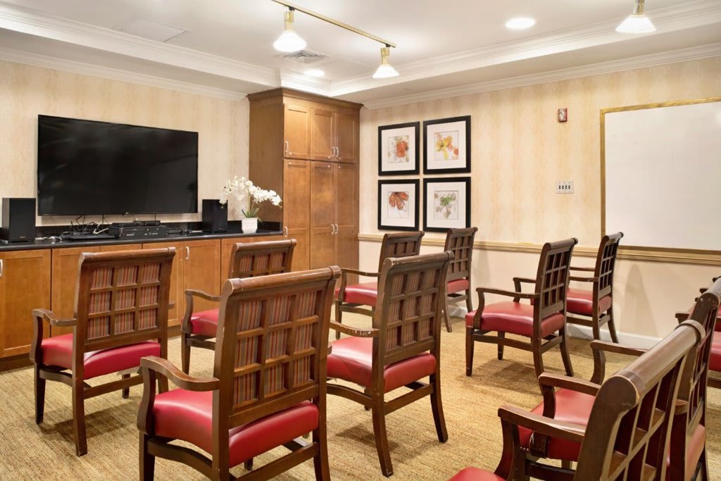 A small conference room with neatly arranged chairs facing a television and decorated walls.
