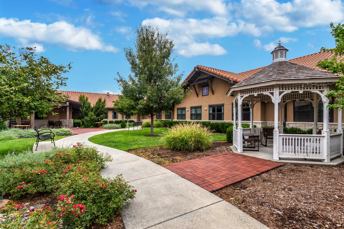 A peaceful courtyard with a gazebo and well-maintained landscaping, featuring a winding pathway under a partly cloudy sky.