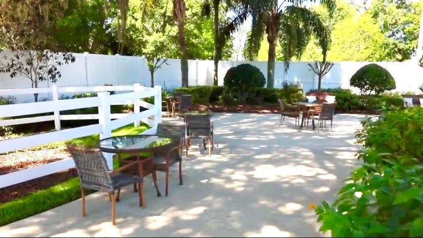 A serene outdoor patio area with tables, chairs, and surrounding trees providing shade.