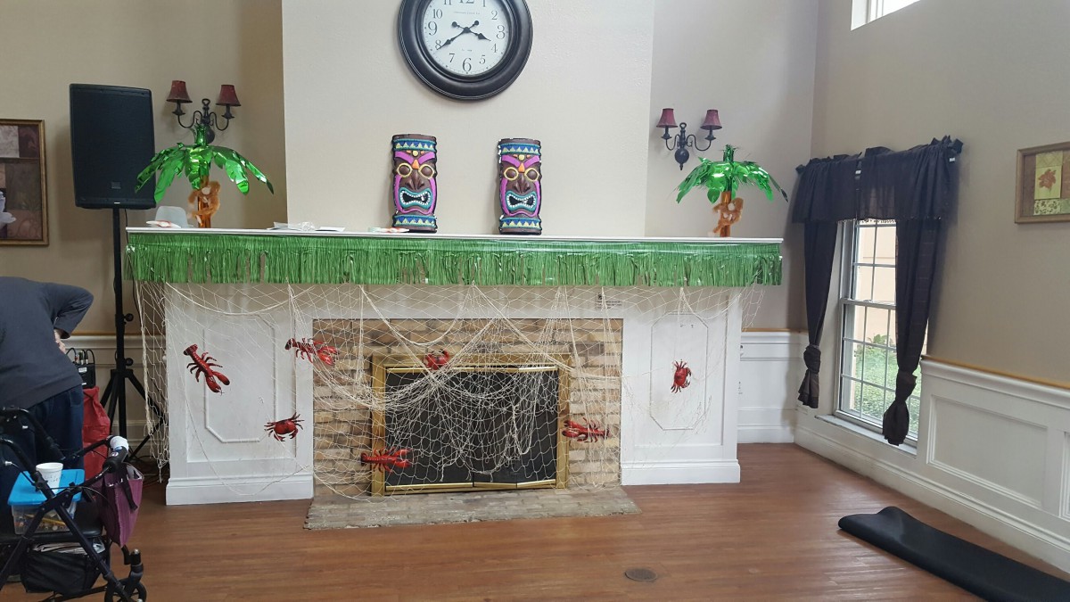 A fireplace adorned with tiki-themed decorations, featuring a clock, green fringe, and spider webs.