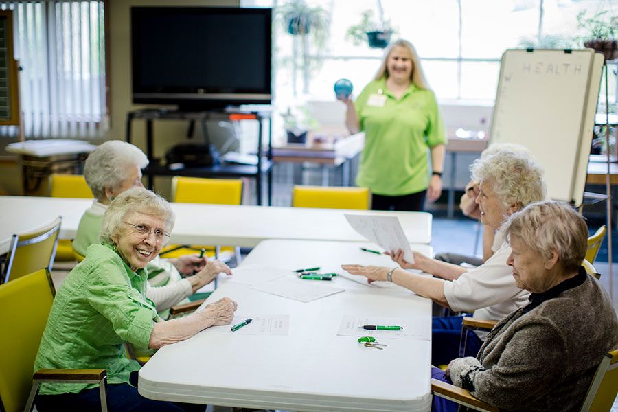 A group of senior citizens enjoying an activity session in a well-lit room with a caregiver.