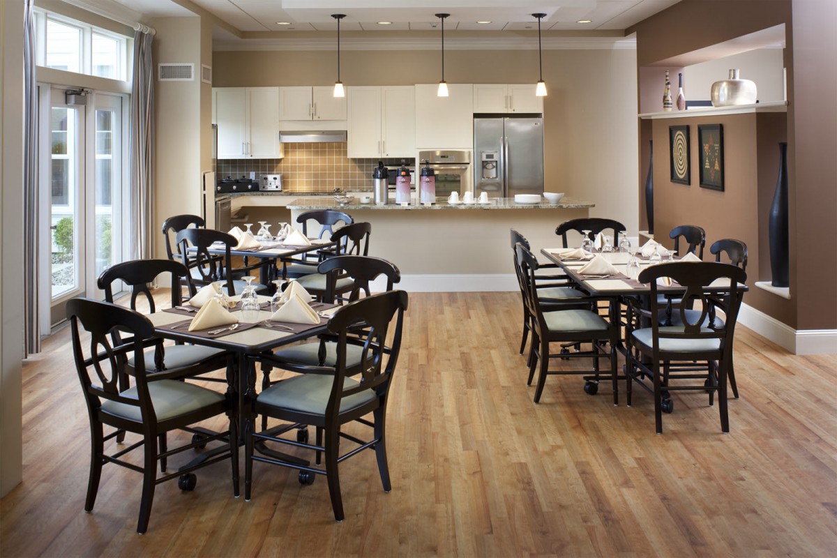 A modern dining area with neatly arranged tables and chairs, featuring a sleek kitchen in the background.
