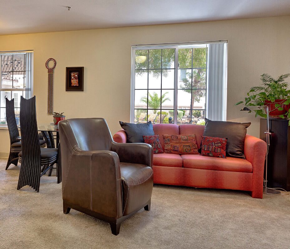 A cozy living room with a red sofa and brown armchair, adjacent to a dining area.