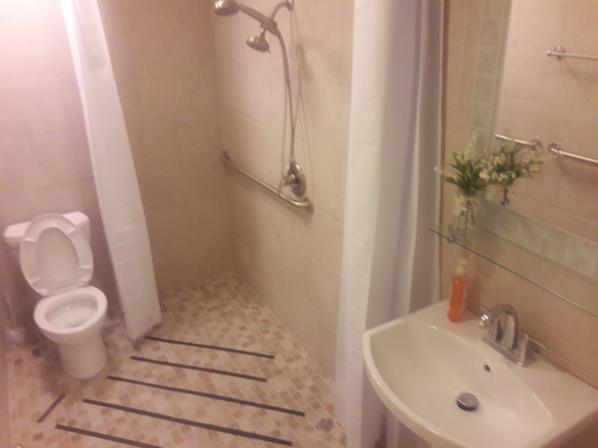A small bathroom featuring a shower area, sink, and toilet with decorative tiles and toiletries.