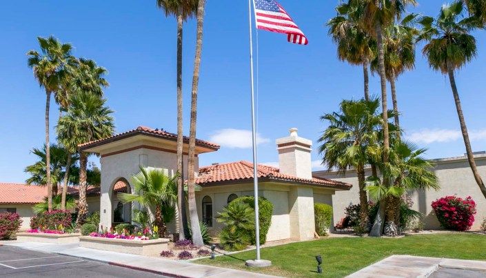 A house with an American flag and palm trees under a clear, sunny sky.