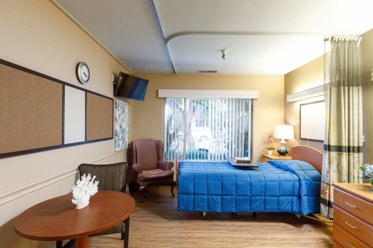 A well-lit hospital room with a single bed, TV, and seating area.