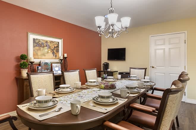 A formal dining room with a large table set for a meal, featuring elegant place settings and decorative artwork on the walls.