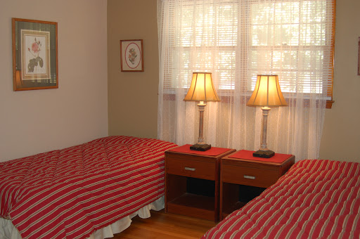 A cozy bedroom featuring twin beds with striped red bedspreads and classic nightstands with lamps.