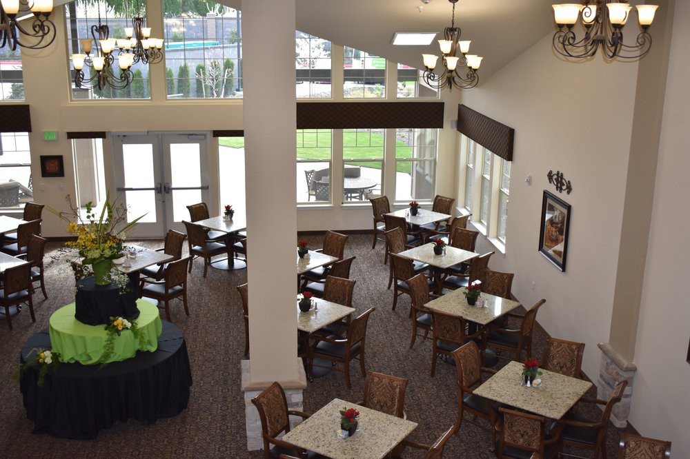 A bright dining area with tables and chairs arranged neatly under chandeliers, featuring large windows that let in natural light.