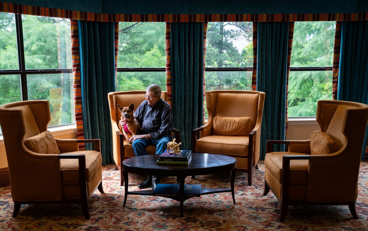 A man and a child sit together in a cozy room with large windows and comfortable armchairs.