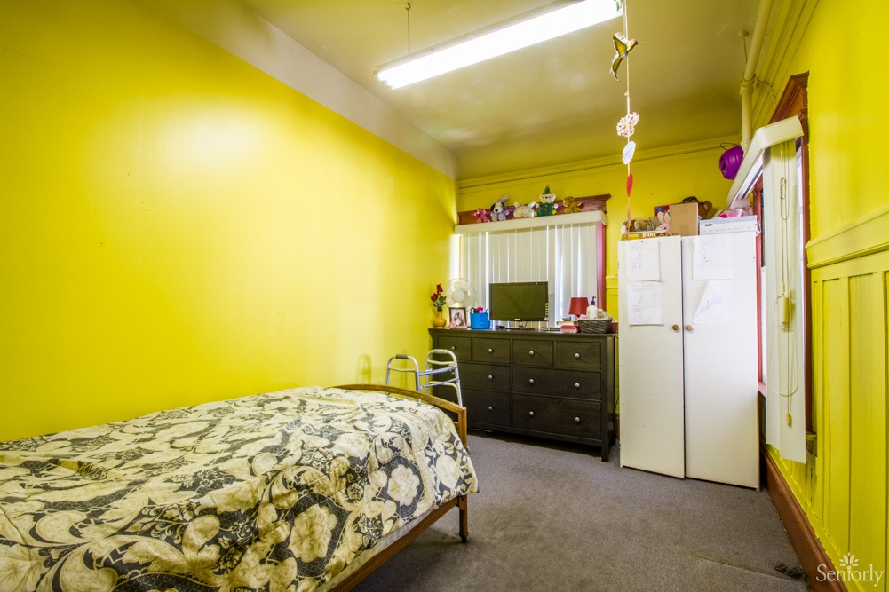 A modest bedroom with yellow walls, featuring a single bed, dresser, and mirror.