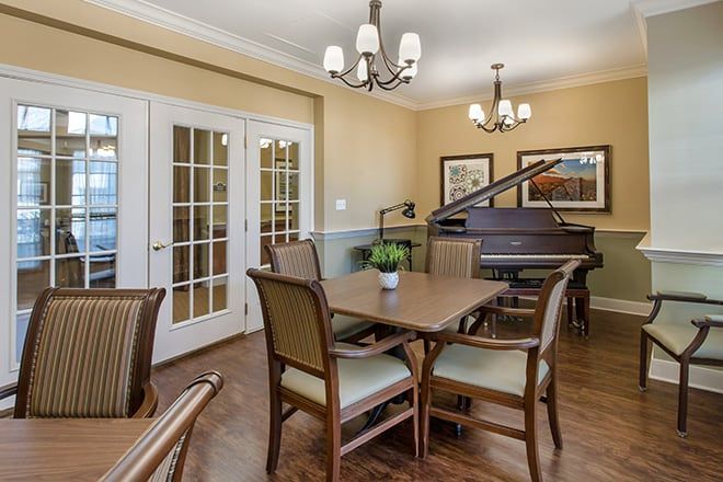 A cozy dining room featuring a grand piano, elegant chandeliers, and French doors.