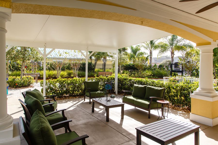A cozy outdoor patio with comfortable seating under a canopy, surrounded by a lush garden.