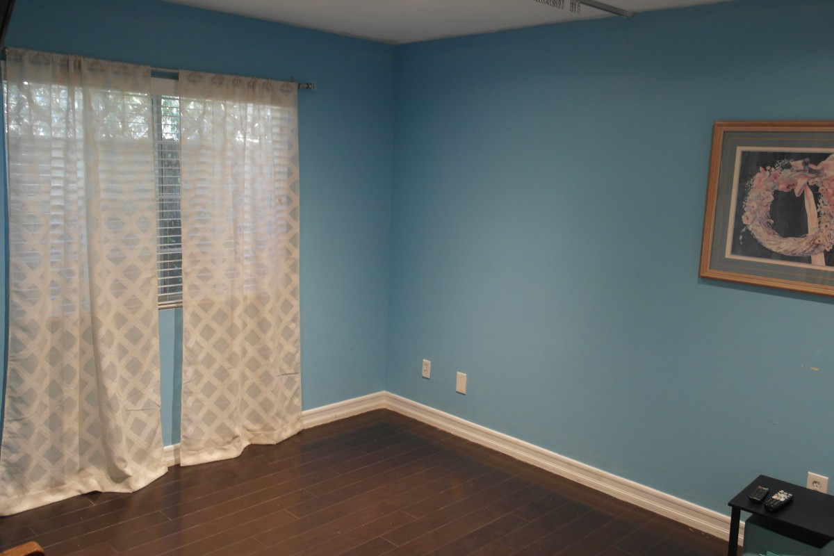A brightly lit room with blue walls, dark wood flooring, and patterned curtains.
