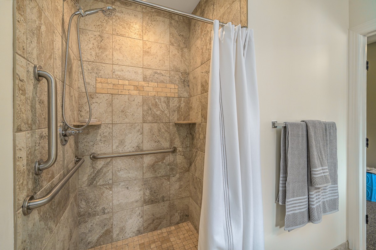 A modern bathroom shower with beige tiles and a white shower curtain.