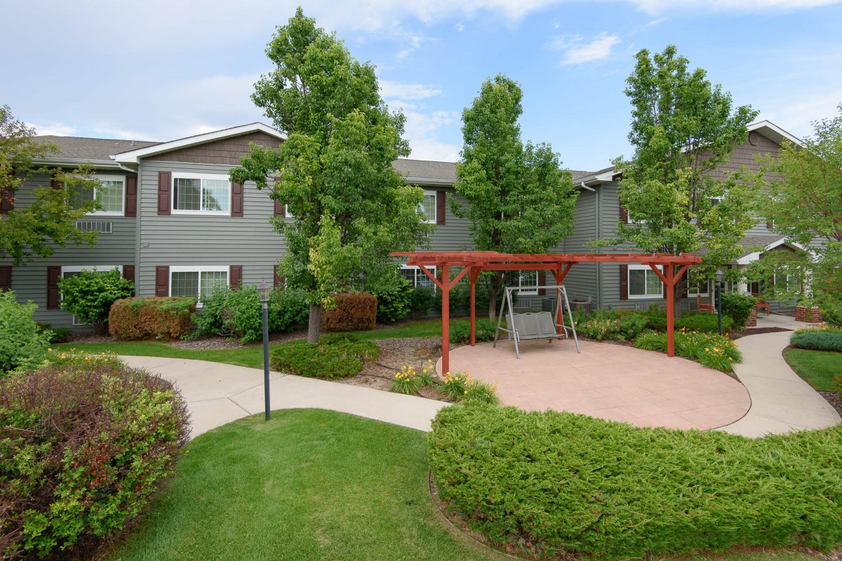 A well-maintained apartment complex with lush landscaping and outdoor swing seating.