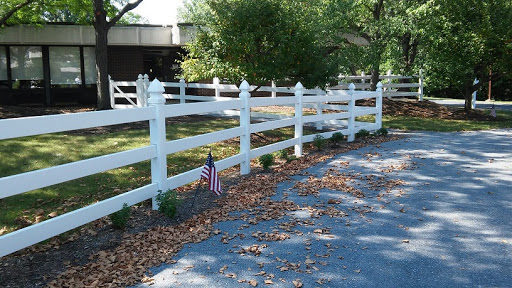 A neatly maintained white fence along a gravel pathway, complemented by seasonal leaves and an American flag.