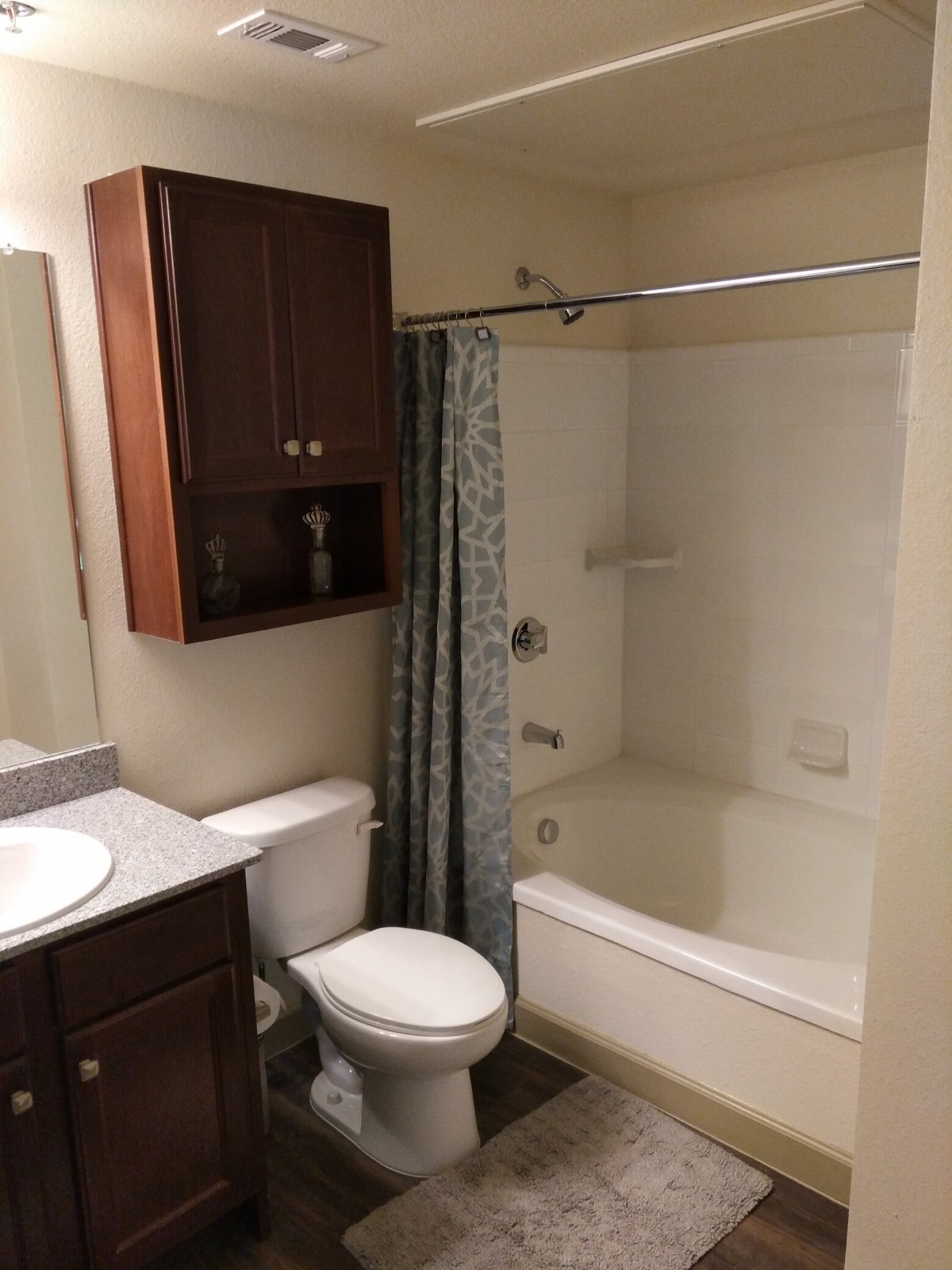 A neatly arranged bathroom featuring a bathtub with a shower curtain, toilet, and vanity sink with a mirror and cabinet.