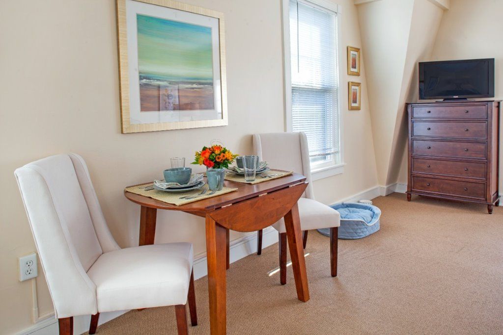 A cozy dining area with a small wooden table set for two, adorned with a colorful centerpiece and artwork on the wall.