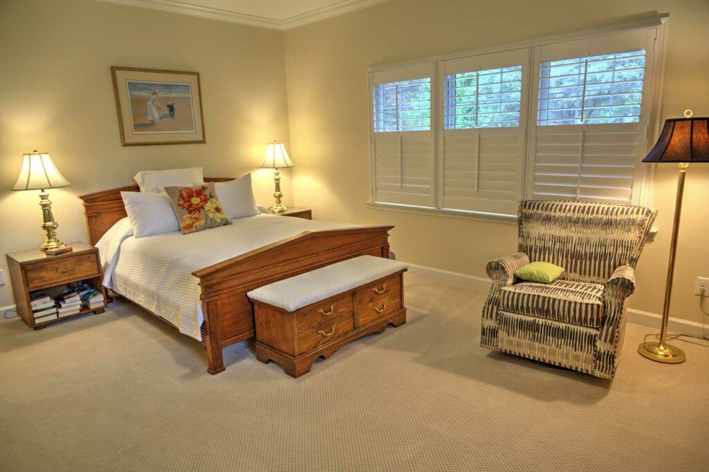 A cozy bedroom with a wooden bed, armchair, and warm lighting.