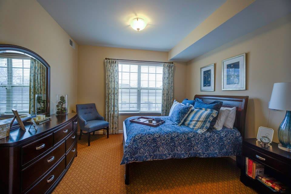 A cozy bedroom with a blue-themed decor, featuring a bed, armchair, and window curtains.