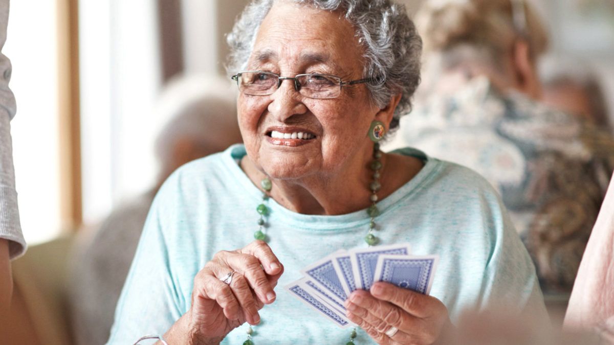An elderly woman smiling while playing cards indoors.