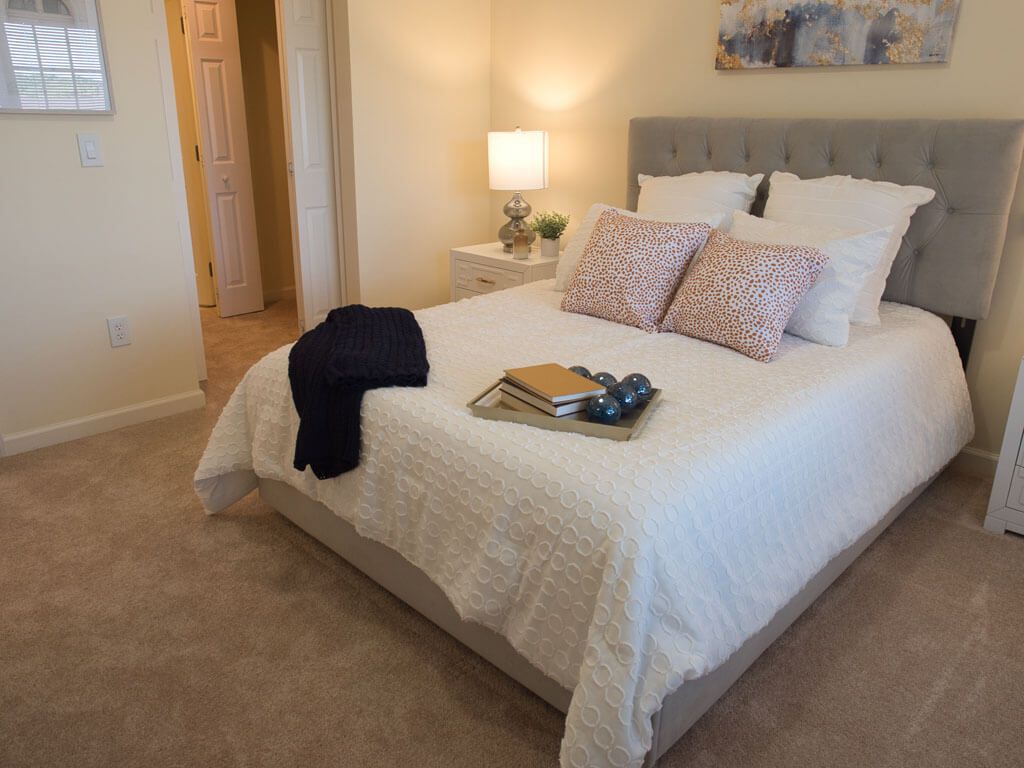 A cozy bedroom interior with a neatly made bed, decorative pillows, and a bedside lamp.