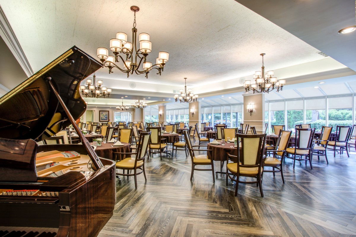 An elegant dining room with a grand piano, chandeliers, and neatly arranged tables and chairs.