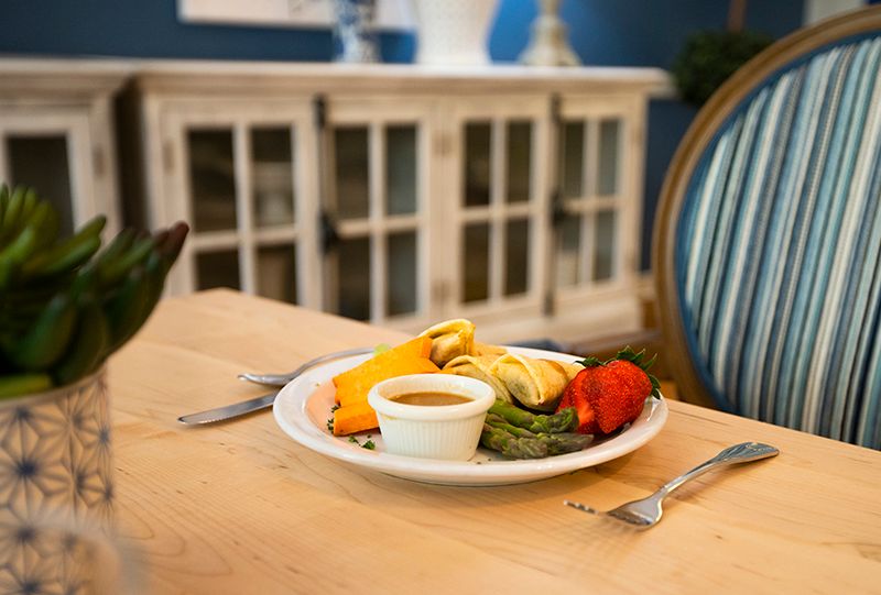A plate of vibrant vegetables with a sauce on a dining table set for a meal.