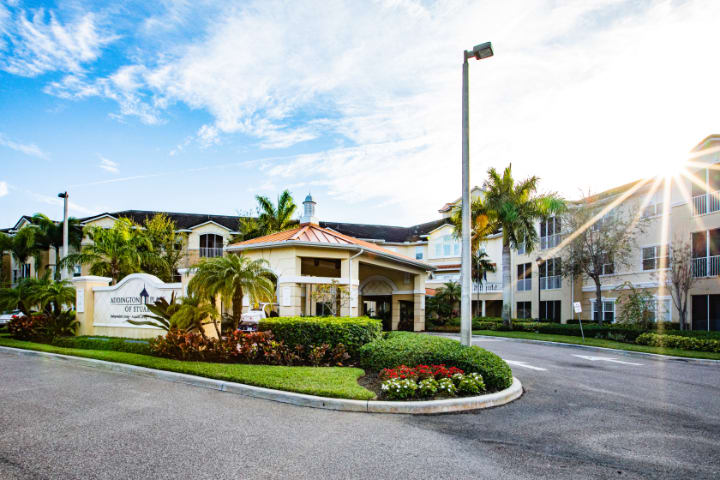 A well-maintained residential entrance with palm trees and lush landscaping under a sunny sky.