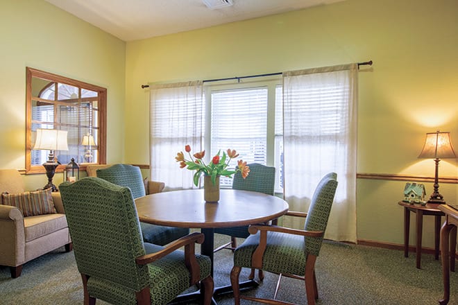 A cozy dining room with a round table, chairs, and a vase of flowers by the window.