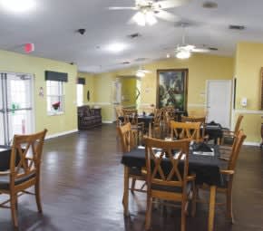 An empty dining room with wooden tables and chairs, ceiling fans, and a wooden floor.